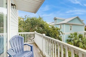 A balcony with a blue Adirondack chair, white railing, and a view of a light blue house with a white roof. - Cloisters on the Ocean 326 (Myrtle Beach)