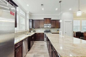 A modern kitchen with dark wood cabinets, stainless steel appliances, and a large island with a marble countertop. - Cloisters on the Ocean 326 (Myrtle Beach)