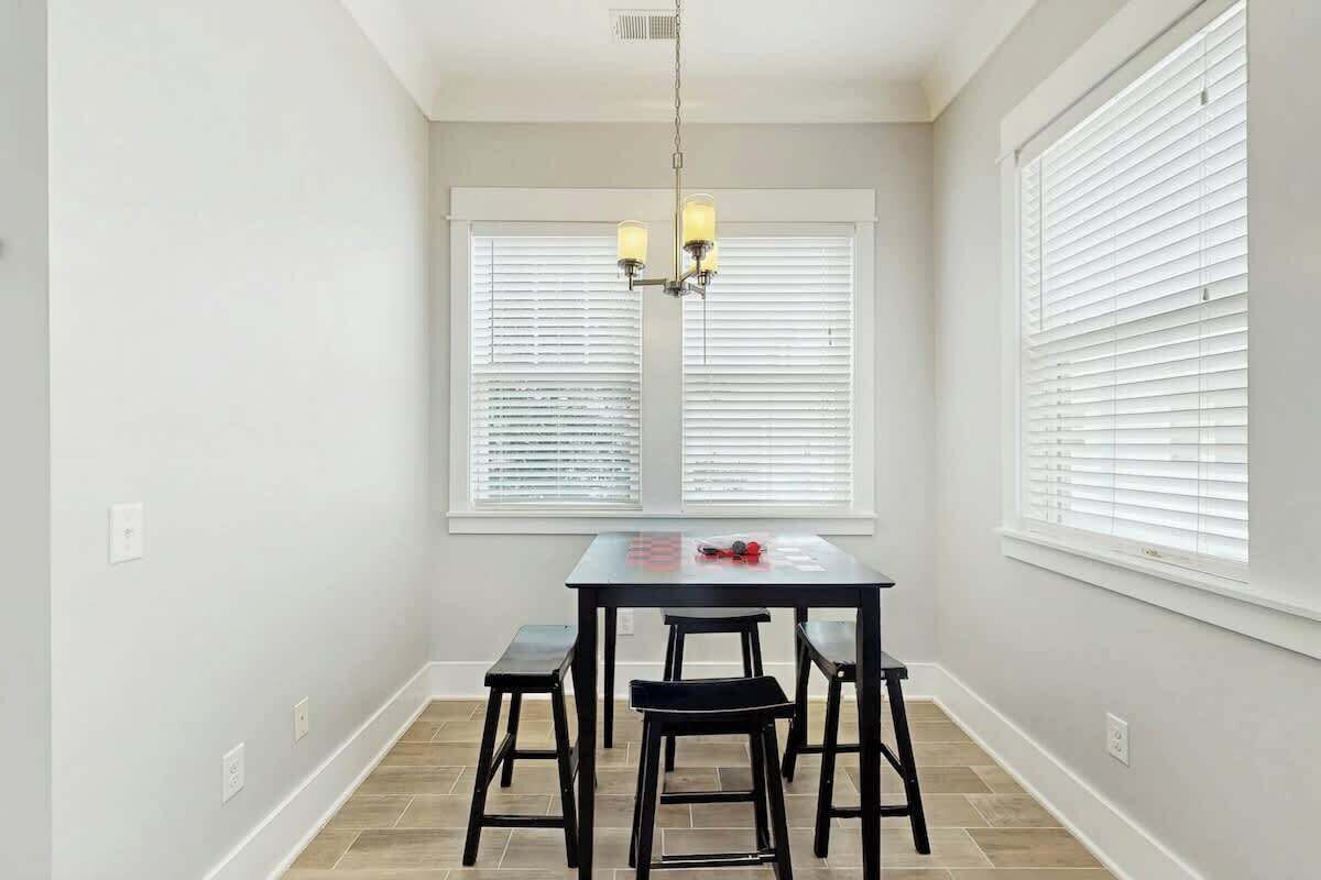 A dining area with a table and four chairs, a chandelier, and two windows with blinds.