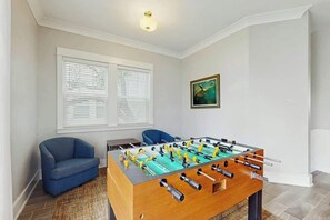 A room with a foosball table, a blue armchair, and a window with blinds. - Cloisters on the Ocean 326 (Myrtle Beach)