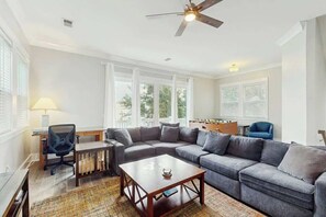 Ein Wohnzimmer mit Ecksofa, Couchtisch, Schreibtisch mit Stuhl und Deckenventilator.