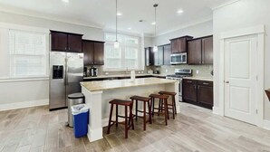 A modern kitchen with a central island, dark wood cabinets, stainless steel appliances, and pendant lighting. - Cloisters on the Ocean 326 (Myrtle Beach)