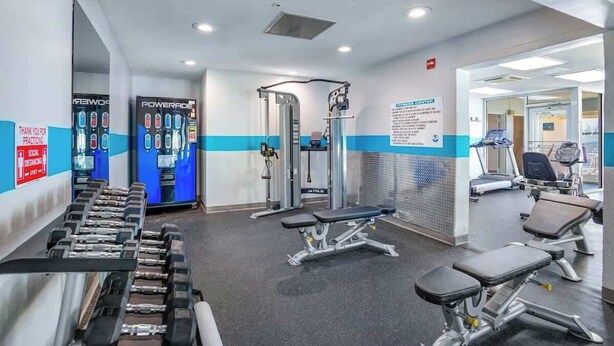 Ein Fitnessstudio mit Trainingsgeräten, darunter Hanteln, Bänken und Kraftmaschinen.