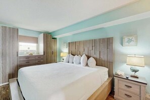 Ein Hotelzimmer mit einem großen Bett, Nachttischen, einem Kleiderschrank und einem Fenster mit Vorhängen.