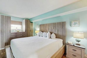 A hotel room with a large bed, a nightstand, a dresser, and a mirror. - Bay Watch Resort 0538 (North Myrtle Beach)