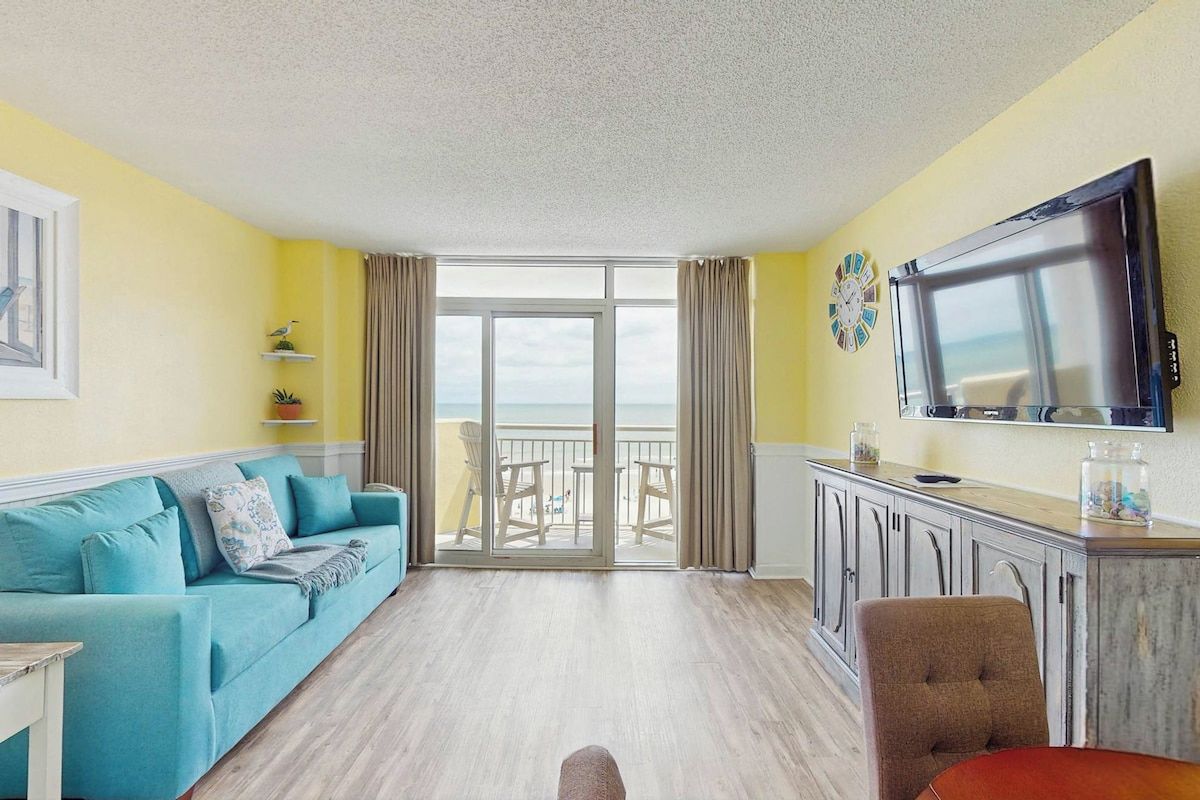 A room with a sofa, a TV, a dining table, and a view to the outside.