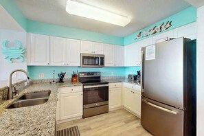 A kitchen with white cabinets, a stainless steel refrigerator, a microwave, and a double oven. - Ashworth Unit 1305 Condo (North Myrtle Beach)