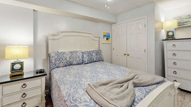 A bedroom with a bed, a nightstand, a dresser, a ceiling fan, and a door. - Ashworth Unit 1305 Condo (North Myrtle Beach)
