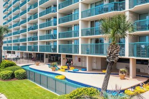 A hotel with multiple balconies, a swimming pool, and a palm tree. - Ashworth Unit 1305 Condo (North Myrtle Beach)