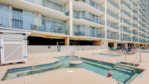 A hotel pool area with multiple levels of balconies, a pool with a diving board, and lounge chairs. - Ashworth Unit 1305 Condo (North Myrtle Beach)