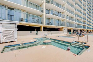 A hotel pool area with multiple levels of balconies, a pool with a diving board, and lounge chairs. - Ashworth Unit 1305 Condo (North Myrtle Beach)