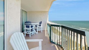 A balcony with a table and chairs, overlooking a beach. - Ashworth Unit 1305 Condo (North Myrtle Beach)