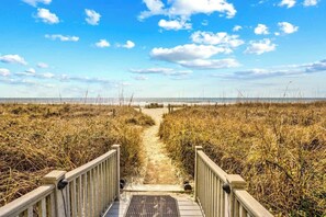 Ein Weg, der zu einem Strand führt, gesäumt von einem Holzzaun auf beiden Seiten.