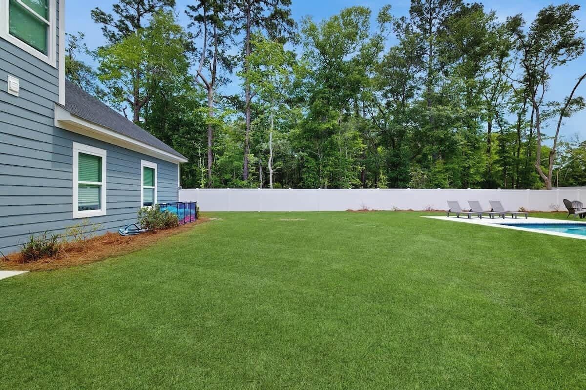 A backyard with a swimming pool, a lawn, and a white fence.
