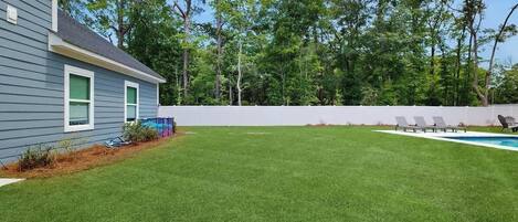 A backyard with a swimming pool, a lawn, and a white fence.
