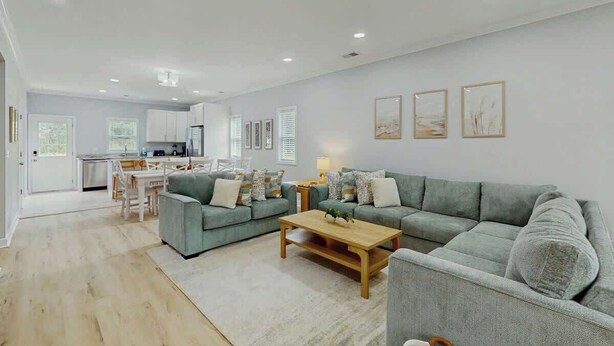 A spacious living area with a grey sofa set, a wooden coffee table, and a dining area with a white table and chairs. - Pawleys Paradise Retreat (Pawleys Island)