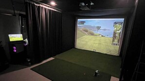 A room with a large screen displaying a video game, a small table with a computer, and a green carpet. - Pawleys Paradise Retreat (Pawleys Island)