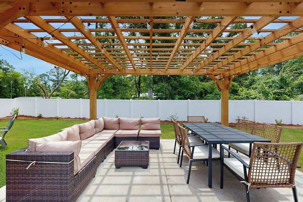An outdoor patio with a pergola, a sectional sofa, a dining table, and wicker chairs.
