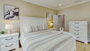 A bedroom with a bed, bedside tables, a dresser, and wall art. - Pawleys Paradise Retreat (Pawleys Island)