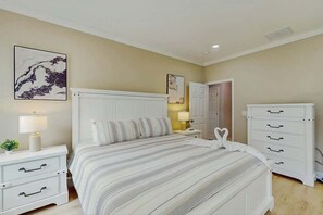A bedroom with a bed, bedside tables, a dresser, and wall art. - Pawleys Paradise Retreat (Pawleys Island)
