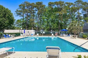 A swimming pool with lounge chairs and umbrellas, surrounded by trees. - Robbers Roost Unit 831 (North Myrtle Beach)