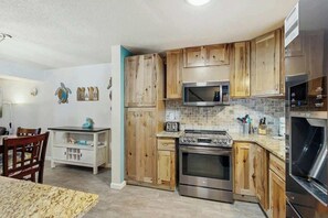 A kitchen with wooden cabinets, a microwave, a stove, and a refrigerator. - Robbers Roost Unit 831 (North Myrtle Beach)