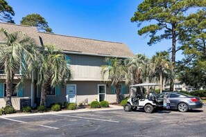 A building with a parking lot, a golf cart, and palm trees. - Robbers Roost Unit 831 (North Myrtle Beach)