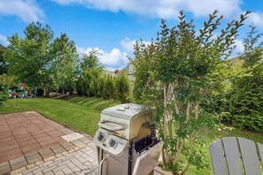 A patio area with a barbecue grill, a wooden chair, and a well-maintained lawn. - Robbers Roost Unit 831 (North Myrtle Beach)