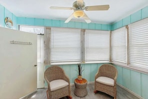 A room with teal walls, a ceiling fan, two wicker chairs, a small table with a plant, and a white door. - Robbers Roost Unit 831 (North Myrtle Beach)