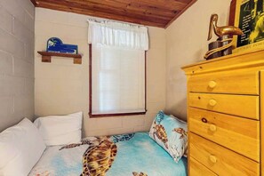 A bedroom with a bed, a dresser, a window with blinds, and a wall-mounted shelf with a decorative item. - Williams Beach Bunker A (North Myrtle Beach)