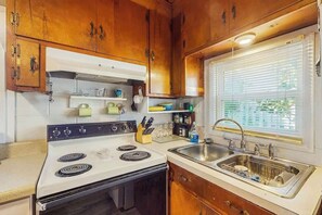 A kitchen with wooden cabinets, a white stove, and a window with blinds. - Williams Beach Bunker A (North Myrtle Beach)