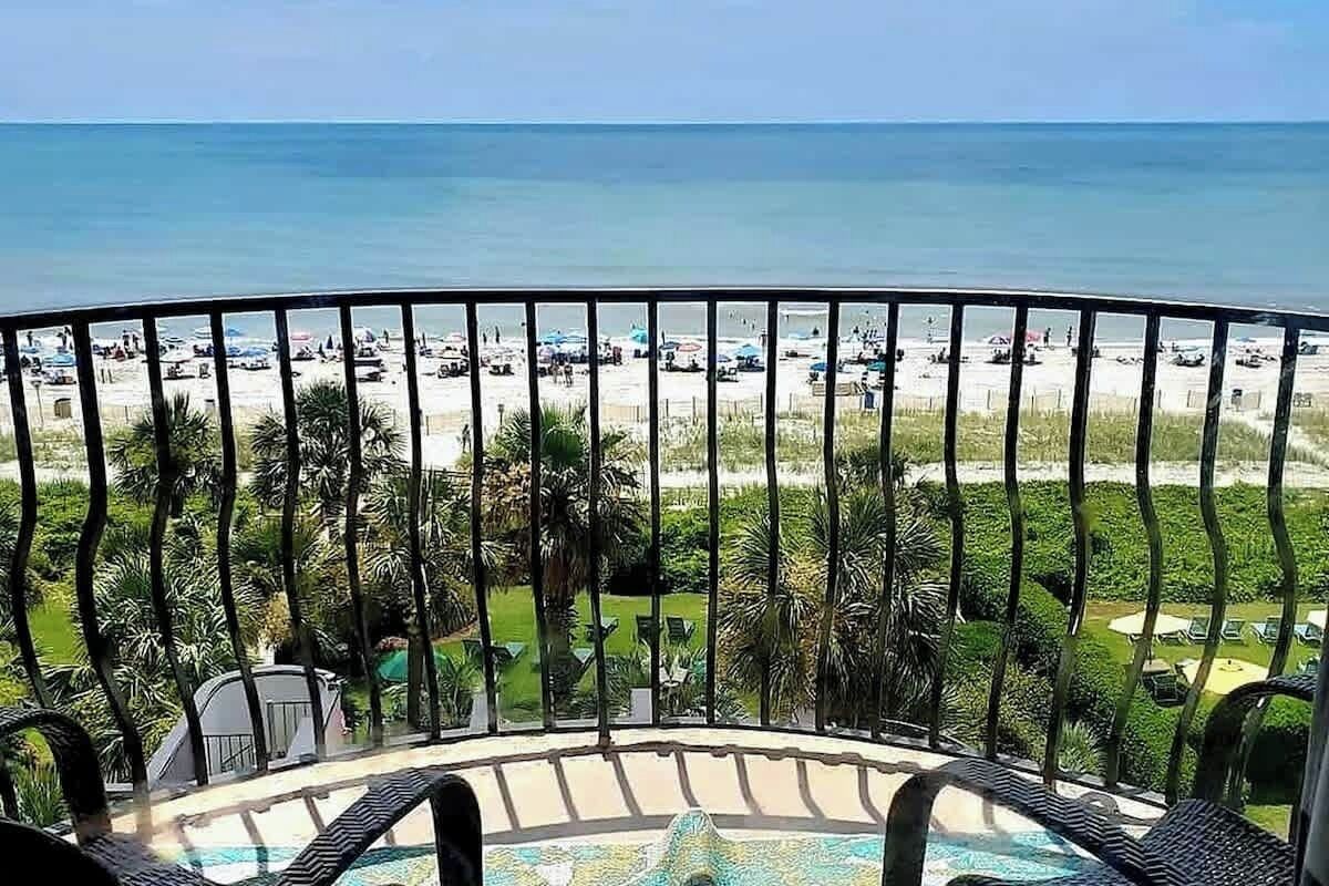 Un balcón con vista a la playa y la piscina.