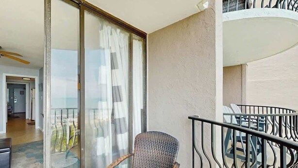 A balcony with a wicker chair and a small table, a glass door leading to a room, and a view of the outdoors. - Palms Resort Unit 404 (Myrtle Beach)