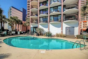 A hotel with a swimming pool, multiple balconies, and palm trees. - Palms Resort Unit 404 (Myrtle Beach)