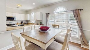 A modern kitchen with white cabinets, a wooden dining table, and a red bowl. - Wild Iris Unit 101 Condo (Myrtle Beach)