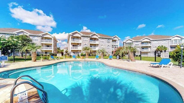 A swimming pool with a clear blue water surface, surrounded by a paved deck. - Wild Iris Unit 101 Condo (Myrtle Beach)
