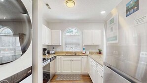 A kitchen with white cabinets, a stainless steel refrigerator, and a window with blinds. - Wild Iris Unit 101 Condo (Myrtle Beach)
