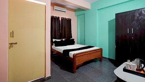 A room with a bed, a wardrobe, a small table with cups and a kettle, and a door.