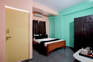 A room with a bed, a wardrobe, a small table with cups and a kettle, and a door.