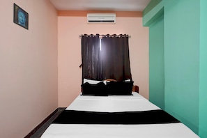 A narrow room with a bed, an air conditioning unit, and a door.