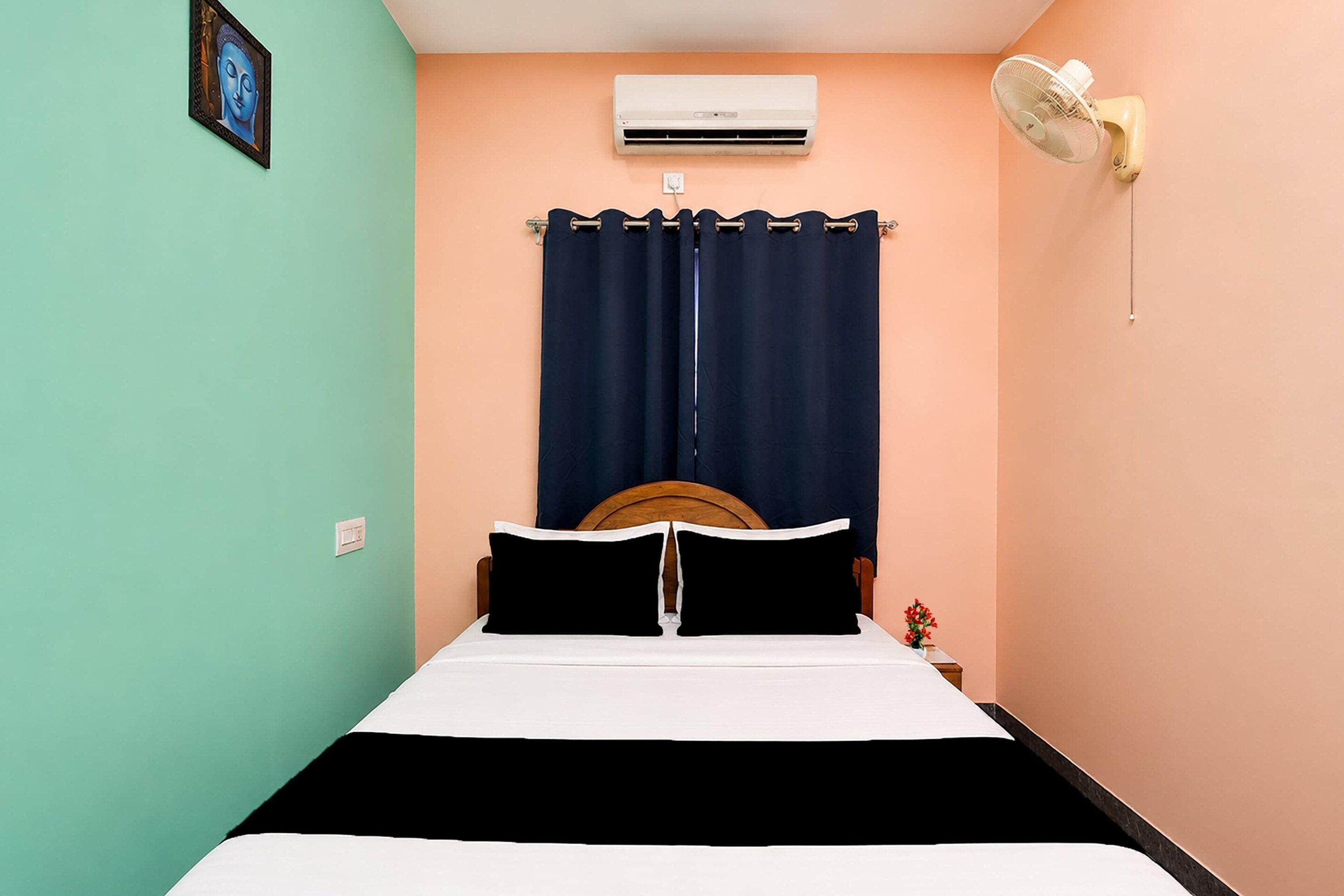 Une chambre à coucher comprenant un lit, un climatiseur, un ventilateur fixé au mur et un rideau.