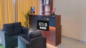 A hotel reception desk with a sign indicating 'HOTEL' and 'OYO-Serviced'. There is a reception area with a sofa and a potted plant. - Hotel O Doddabalapura (Doddaballapur)