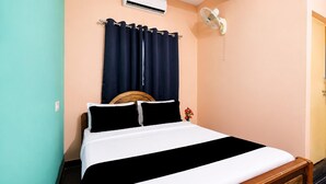 A single bed with a wooden headboard, a white and black bedspread, and a dark blue curtain.