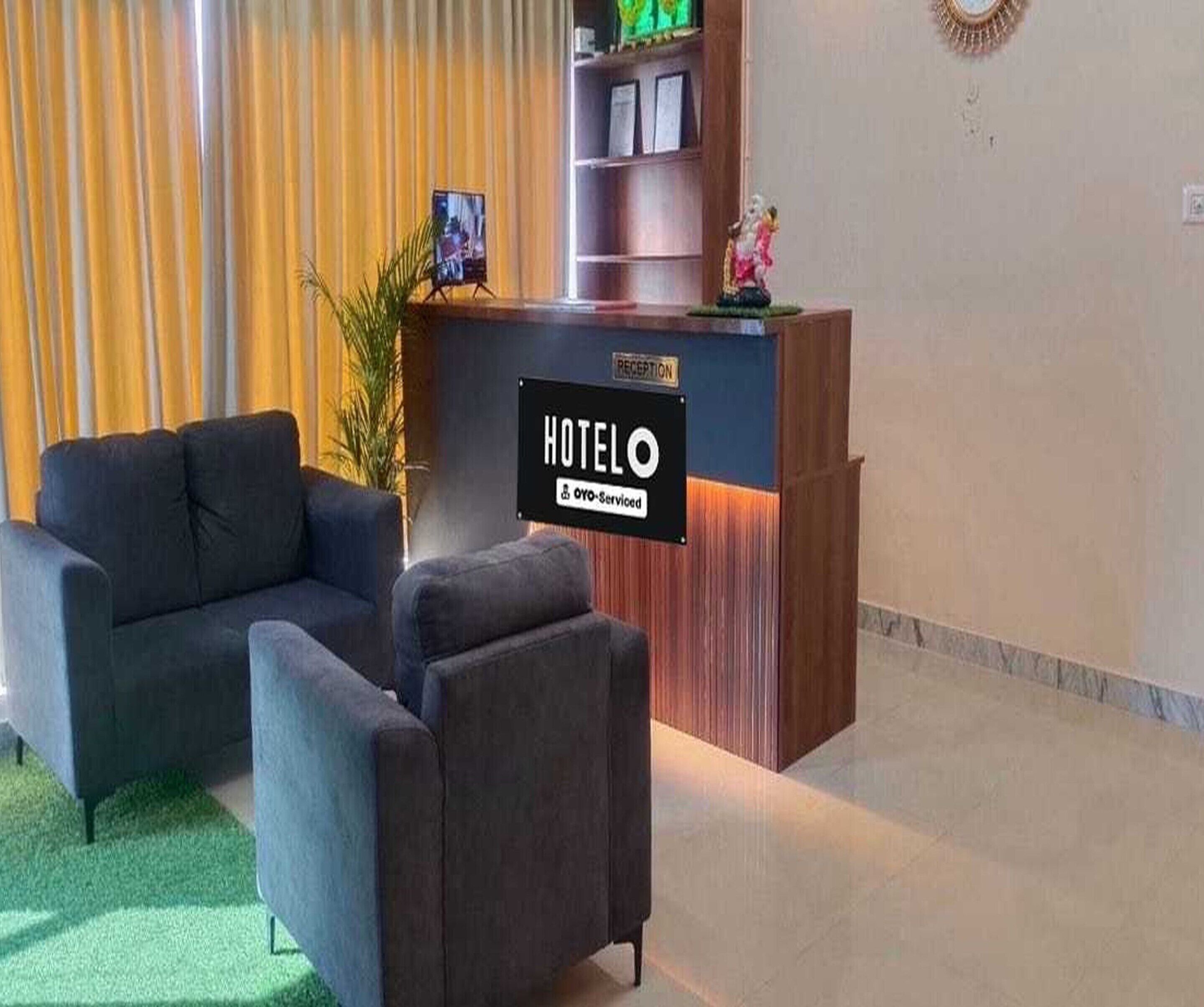 A hotel reception desk with a sign indicating it is serviced by OYO. There are two sofas in the foreground.