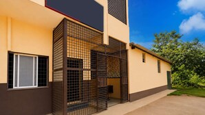 A modern building with a gated entrance, a window with a metal grille, and a door with a patterned curtain.