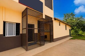 A modern building with a gated entrance, a window with a metal grille, and a door with a patterned curtain.