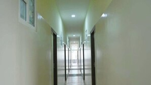 A long, narrow hallway with doors on both sides, leading to an open area at the end. - Hotel O Doddabalapura (Doddaballapur)