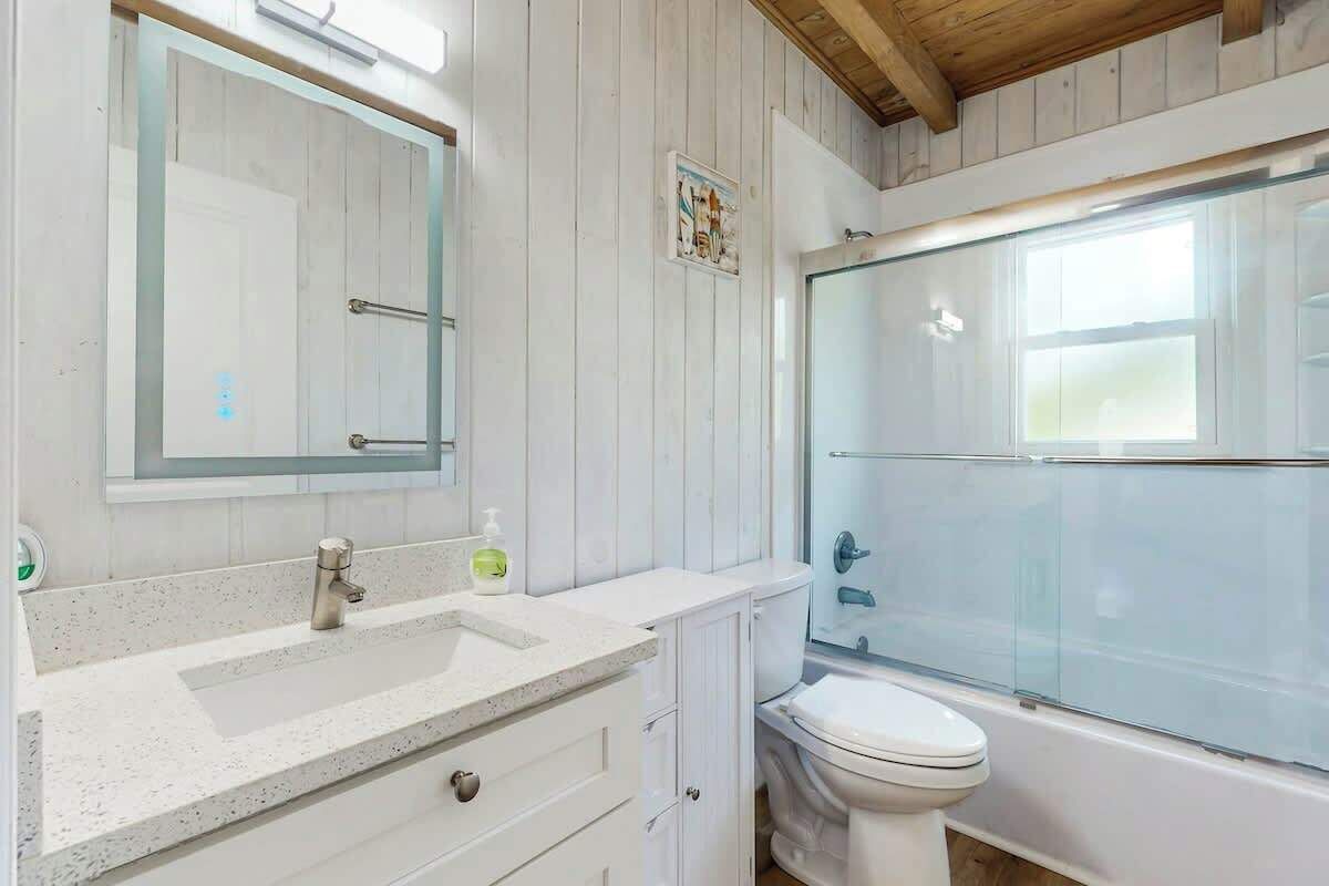 Een badkamer met een douchecabine van glas, een witte wastafel met zeepdispenser en een toilet.