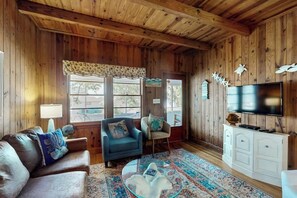 A wooden-paneled room with a leather sofa, two armchairs, a glass coffee table, a patterned rug, a television, and a cabinet. - Williams Beach Bunker B (North Myrtle Beach)