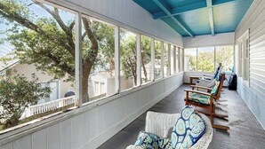 A covered porch with large windows, wicker furniture, and a view of trees and a house. - Williams Beach Bunker B (North Myrtle Beach)